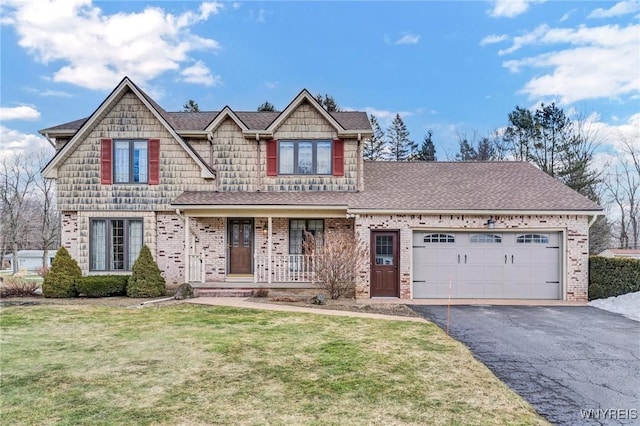 view of front of property featuring brick siding, a front lawn, aphalt driveway, covered porch, and an attached garage