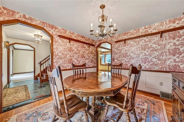 dining room featuring arched walkways, a wainscoted wall, and wallpapered walls