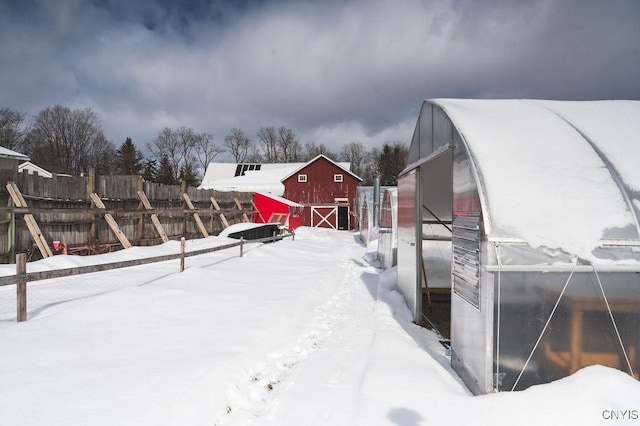 snowy yard with a greenhouse, a barn, an outdoor structure, and fence