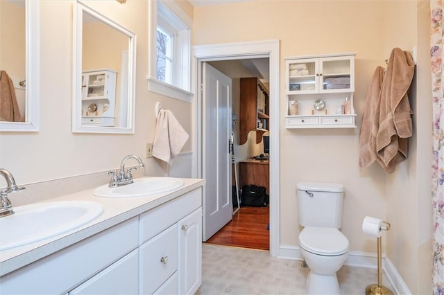 full bath with double vanity, toilet, baseboards, and a sink