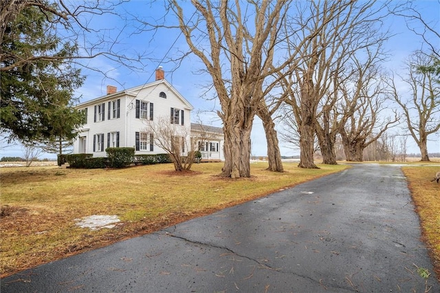 view of front of property with a front lawn, aphalt driveway, and a chimney