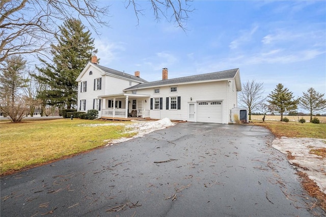 view of front of property with driveway, an attached garage, covered porch, a chimney, and a front lawn