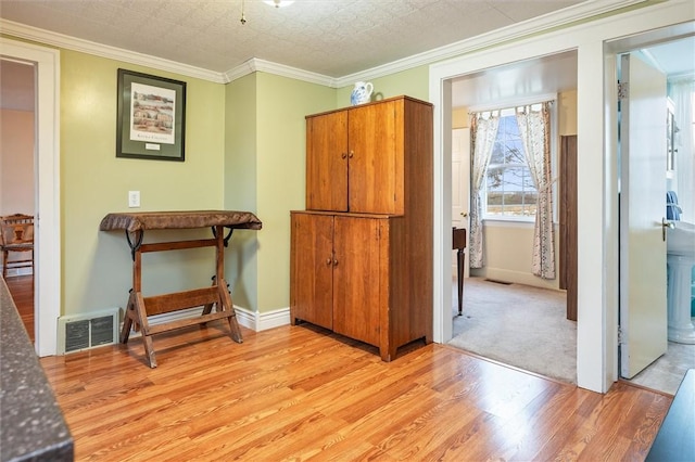 hallway featuring light wood-type flooring, visible vents, baseboards, and crown molding