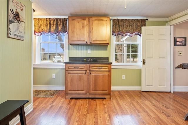 kitchen with dark countertops, crown molding, brown cabinetry, and light wood finished floors