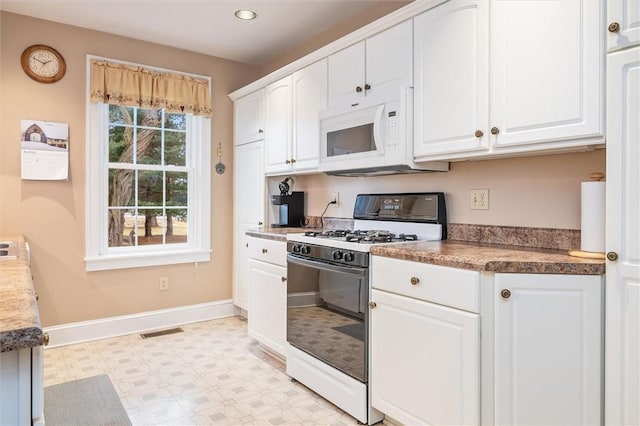 kitchen with white microwave, visible vents, light floors, range with gas stovetop, and white cabinets