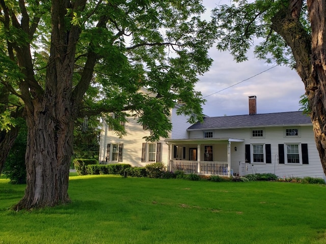 view of front of house featuring a chimney, covered porch, and a front lawn