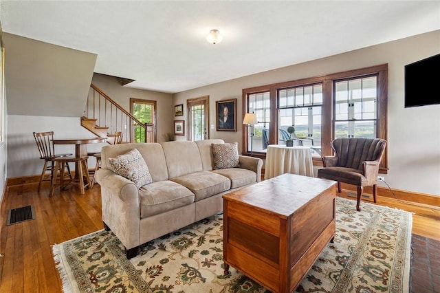 living room with visible vents, baseboards, wood finished floors, and stairway