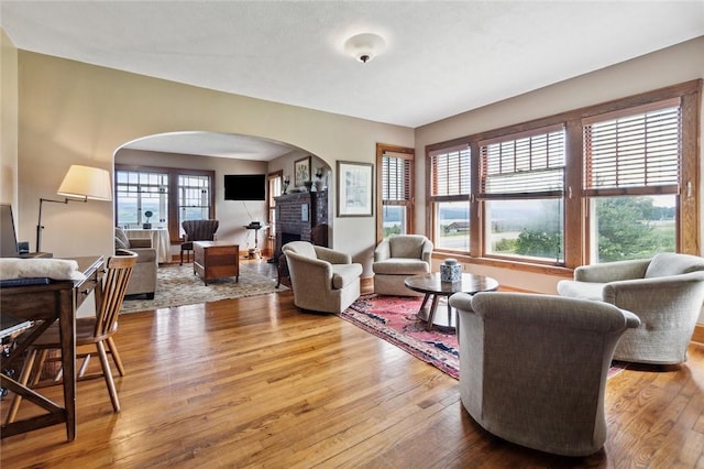 living room featuring arched walkways, a brick fireplace, and hardwood / wood-style floors