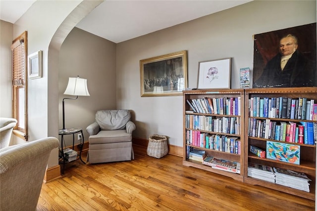 living area with arched walkways, baseboards, and wood finished floors