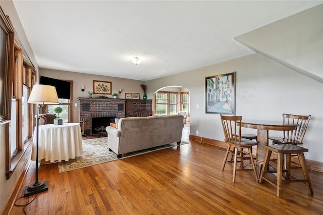 living room with a brick fireplace, wood finished floors, arched walkways, and baseboards