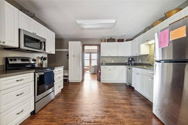 kitchen featuring dark countertops, dark wood-style flooring, appliances with stainless steel finishes, and a sink