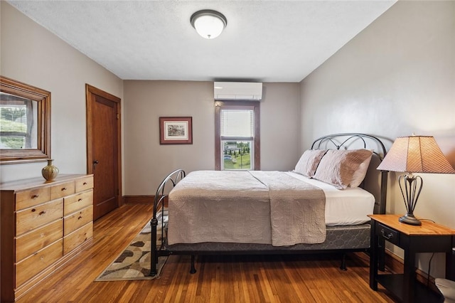 bedroom with a wall mounted AC, baseboards, and hardwood / wood-style flooring