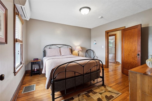 bedroom with visible vents, a wall mounted air conditioner, light wood-type flooring, and baseboards