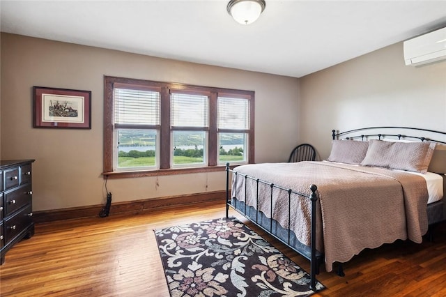 bedroom featuring light wood-style flooring, an AC wall unit, and baseboards