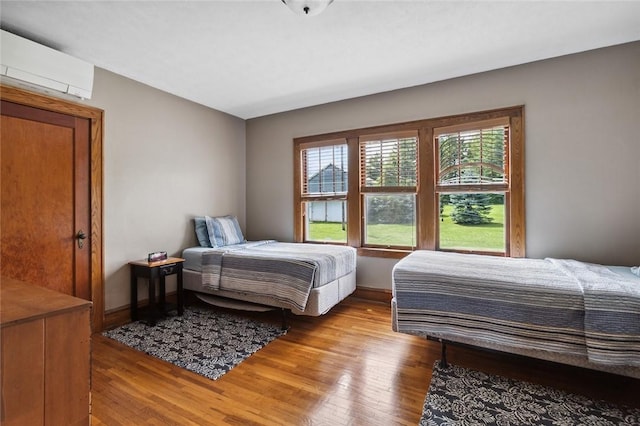 bedroom with hardwood / wood-style floors, baseboards, and a wall mounted air conditioner