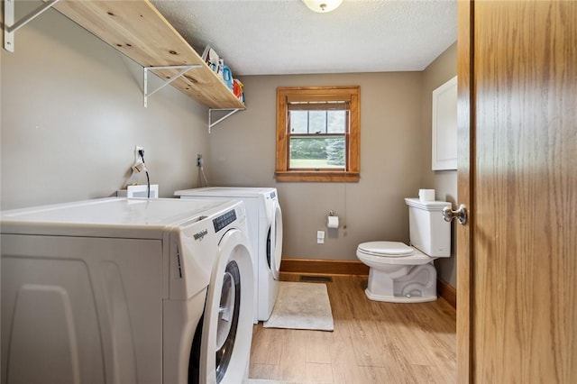 clothes washing area featuring washer and dryer, a textured ceiling, light wood-style floors, baseboards, and laundry area