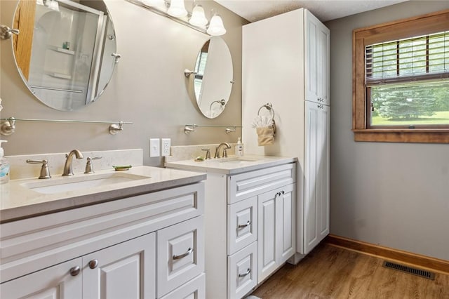 bathroom with visible vents, baseboards, wood finished floors, vanity, and a shower