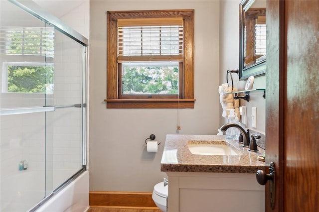 full bathroom featuring toilet, vanity, baseboards, and shower / bath combination with glass door