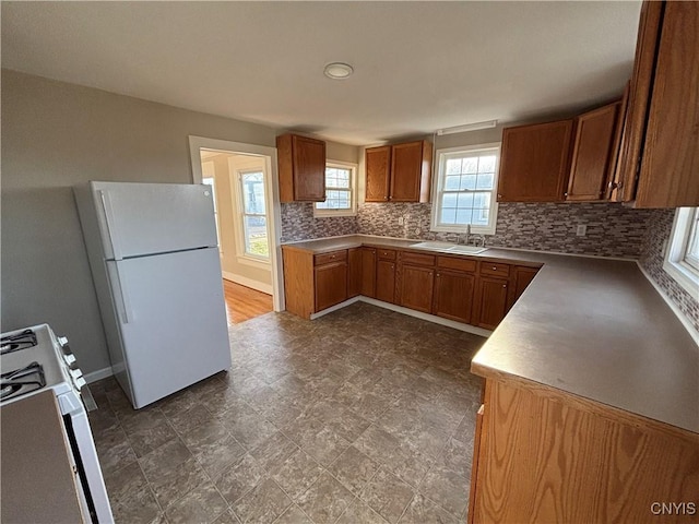 kitchen featuring white appliances, baseboards, brown cabinets, a sink, and tasteful backsplash