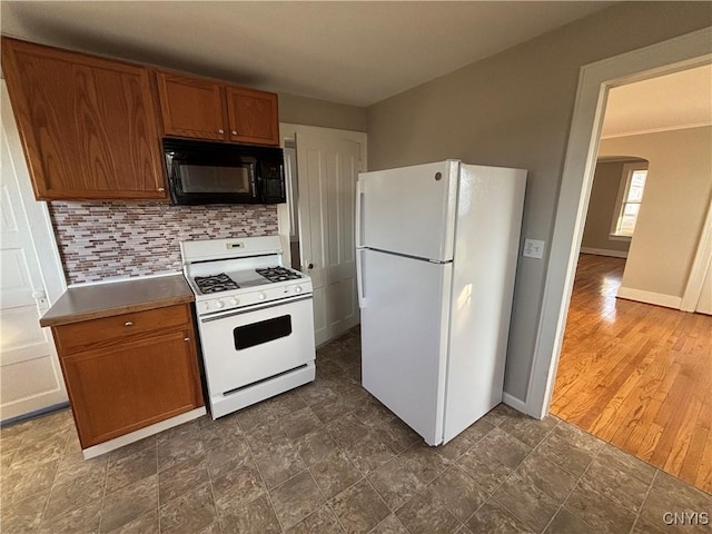 kitchen with baseboards, decorative backsplash, brown cabinets, arched walkways, and white appliances