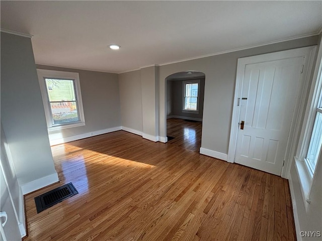 spare room with visible vents, wood finished floors, arched walkways, crown molding, and baseboards