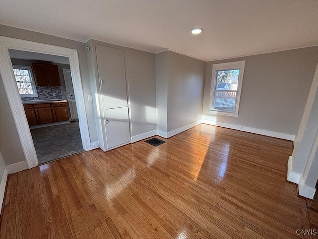 unfurnished bedroom with visible vents, baseboards, wood finished floors, and crown molding