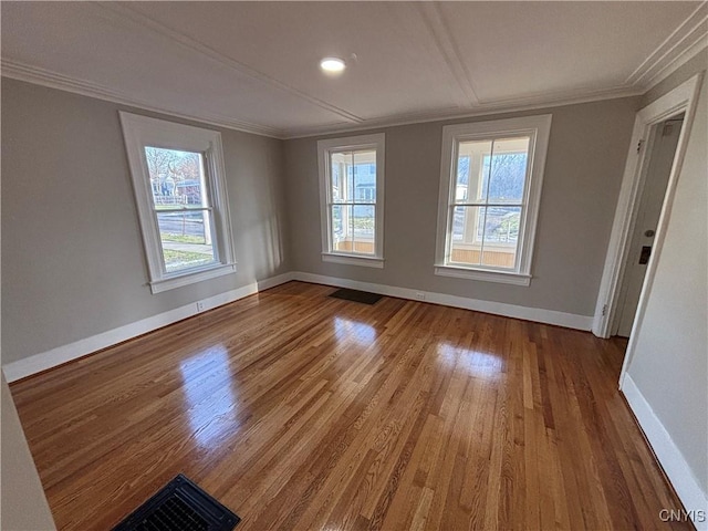 empty room featuring visible vents, wood finished floors, baseboards, and ornamental molding