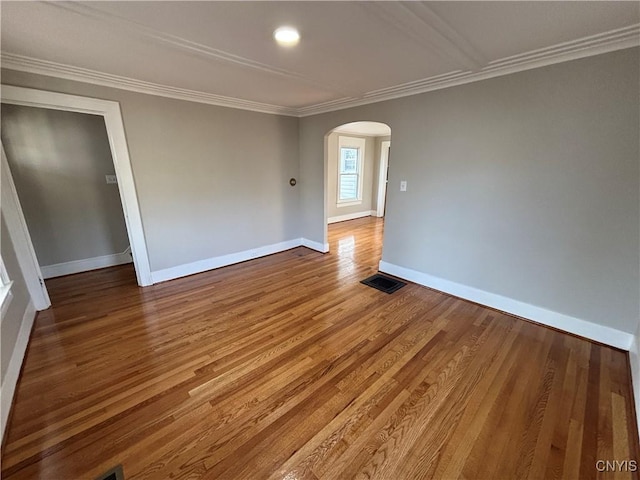 unfurnished room with visible vents, wood finished floors, arched walkways, crown molding, and baseboards