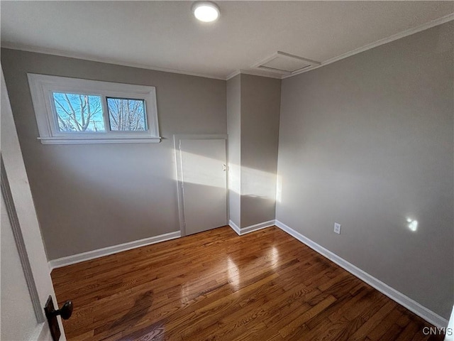 unfurnished bedroom with attic access, crown molding, wood finished floors, and baseboards