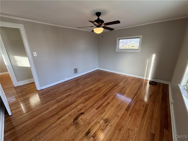 spare room with visible vents, wood finished floors, baseboards, and ornamental molding