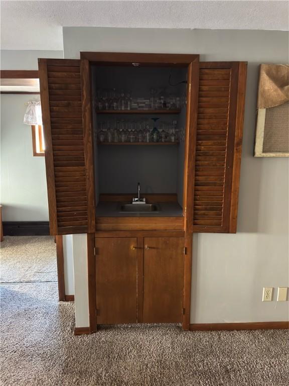 bar with a sink, indoor wet bar, light carpet, and a textured ceiling