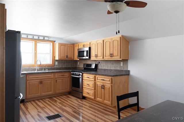 kitchen featuring visible vents, lofted ceiling, decorative backsplash, stainless steel appliances, and a sink