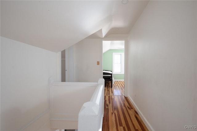 corridor with an upstairs landing, baseboards, lofted ceiling, and wood finished floors