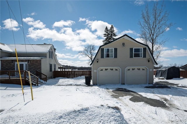 view of snowy exterior featuring a gambrel roof, a garage, and fence