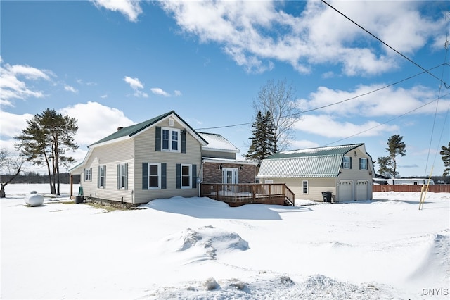 snow covered back of property featuring a deck, a garage, and a gambrel roof