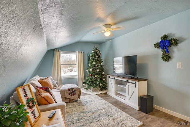 living area with wood finished floors, baseboards, ceiling fan, vaulted ceiling, and a textured ceiling