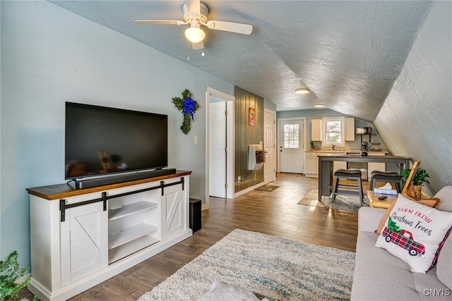 living room featuring wood finished floors, baseboards, lofted ceiling, ceiling fan, and a textured ceiling