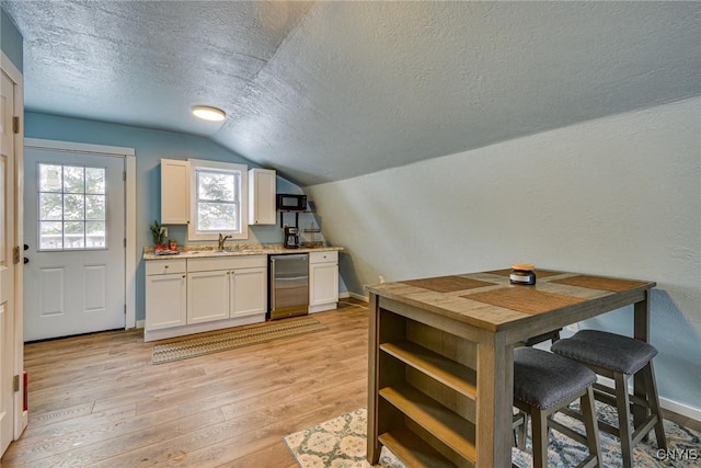 kitchen featuring lofted ceiling, a sink, black microwave, a textured ceiling, and light wood-type flooring