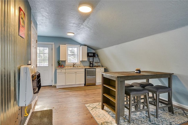 kitchen with light wood-style flooring, a textured ceiling, white cabinets, black microwave, and lofted ceiling