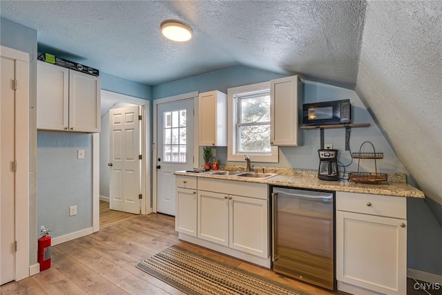 kitchen with a sink, white cabinetry, black microwave, and light wood finished floors