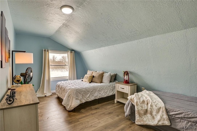 bedroom featuring vaulted ceiling, a textured ceiling, a textured wall, and hardwood / wood-style floors