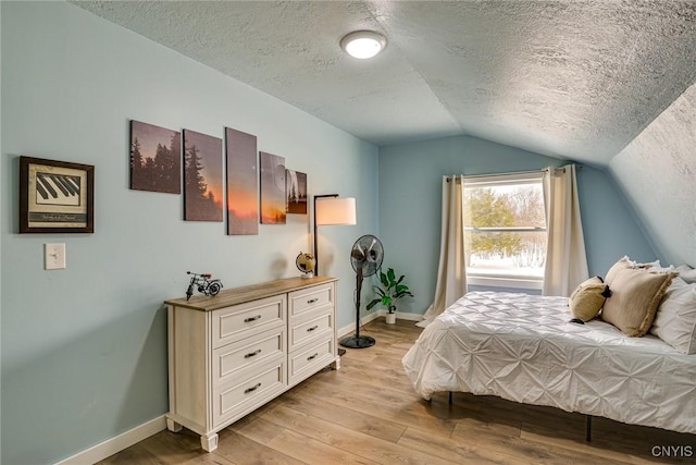 bedroom with baseboards, lofted ceiling, a textured ceiling, and light wood finished floors