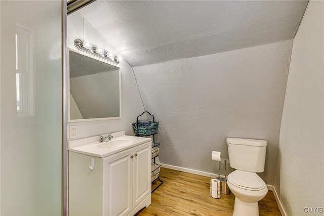 bathroom featuring baseboards, toilet, vaulted ceiling, wood finished floors, and vanity