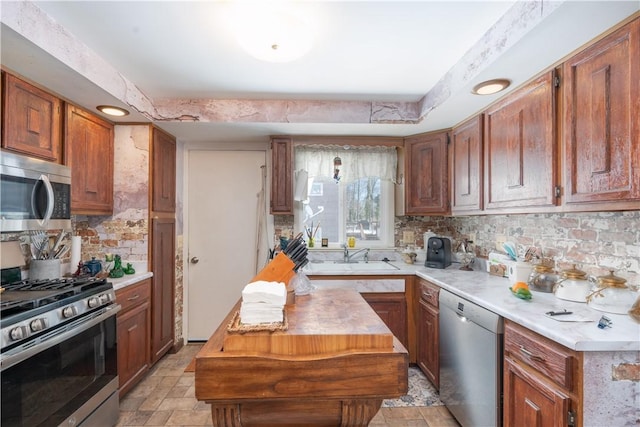 kitchen with brown cabinets, a sink, stone finish flooring, tasteful backsplash, and stainless steel appliances