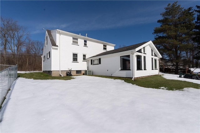 snow covered rear of property featuring central AC and fence