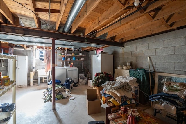 unfinished below grade area with washing machine and clothes dryer, concrete block wall, and freestanding refrigerator