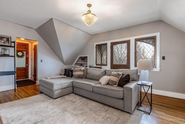 living room with vaulted ceiling, an inviting chandelier, baseboards, and wood finished floors