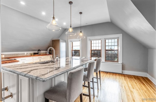 kitchen featuring baseboards, lofted ceiling, light wood-style flooring, a sink, and white cabinets