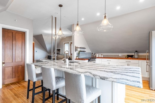 kitchen featuring a sink, light stone counters, white cabinetry, light wood finished floors, and vaulted ceiling