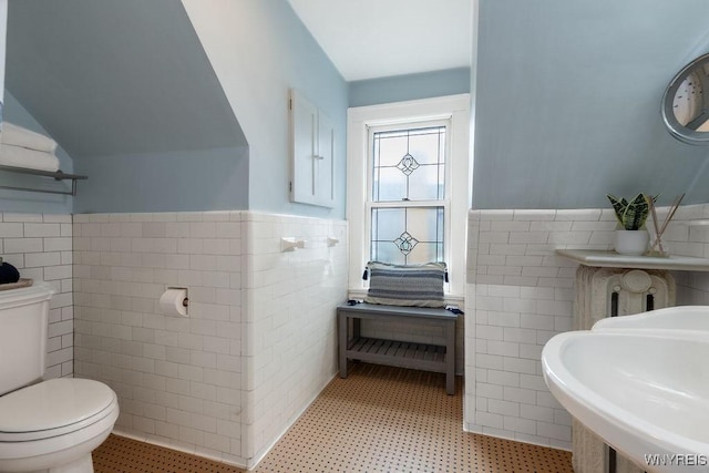 half bath featuring a wainscoted wall, lofted ceiling, a sink, tile walls, and toilet